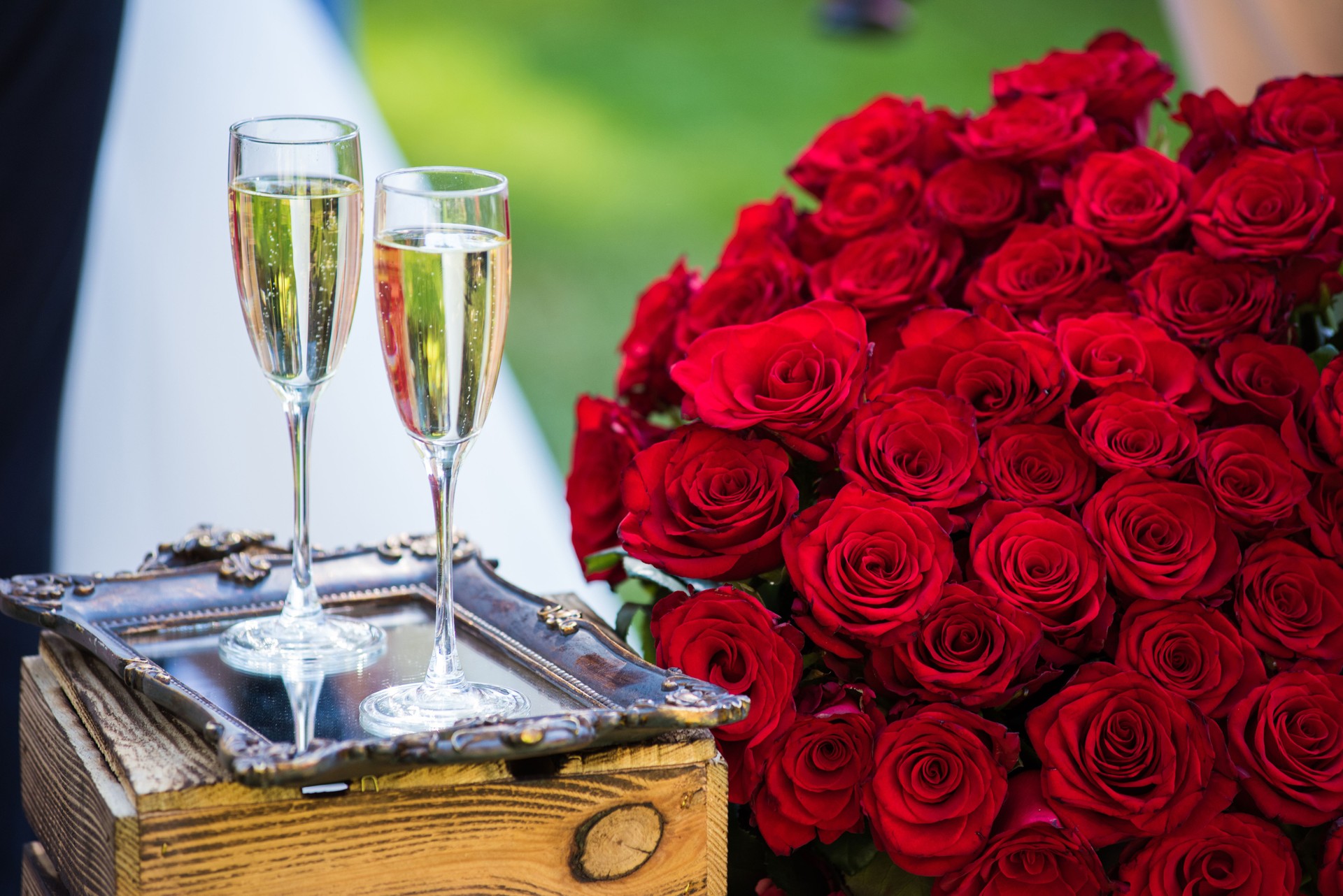 Wedding bouquet of red roses and two champagne glasses standing on the authentic decorative mirror.